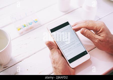 Mains du patient senior remplissant le formulaire d'information en ligne sur son smartphone Banque D'Images