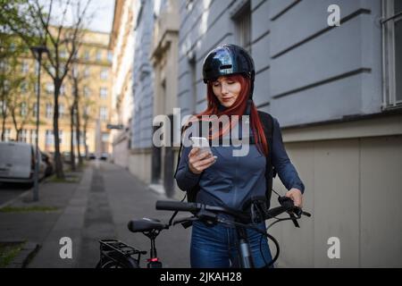 Portrait d'une femme d'affaires en route pour travailler avec un vélo, en utilisant un smartphone, concept de mode de vie durable. Banque D'Images