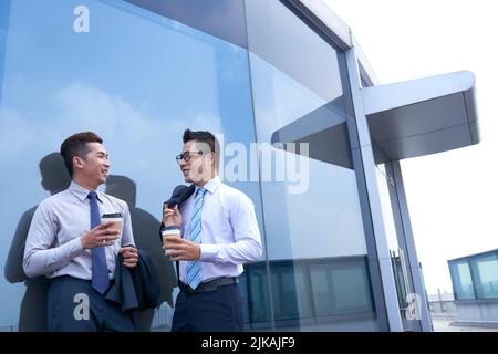 Des collègues joyeux se tenant à l'extérieur, parlant et buvant du café en train de faire une courte pause Banque D'Images