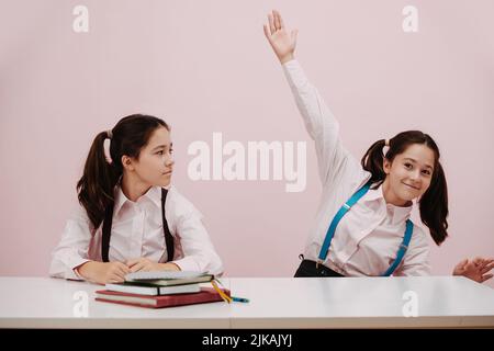 Écolière enthousiaste et perky levant une main, sa jumelle la raquette avec suspense Banque D'Images