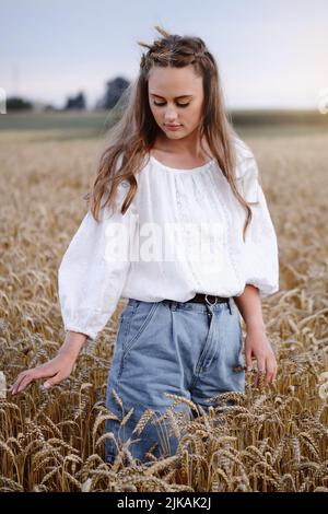 Femme marchant sur le champ doré de blé tenant tas de seigle. Femme tendance touchant un petit-lait en plein air le soir. Beauté du coucher du soleil Banque D'Images