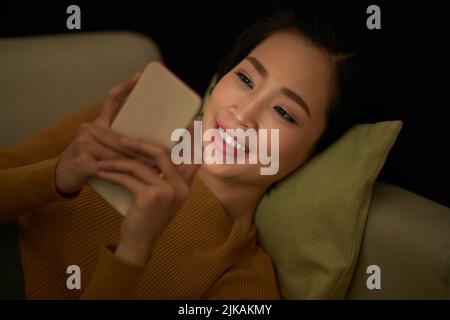 Jeune femme souriante qui vérifie les massages de texte sur son smartphone tard dans la nuit Banque D'Images