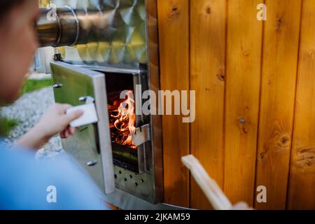 Femme méconnue mettant un morceau de bois dans le bain à remous extérieur. Gros plan. Banque D'Images