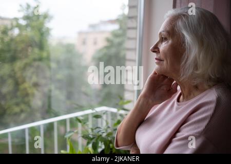 Une femme âgée a l'air tristement par la fenêtre. Banque D'Images