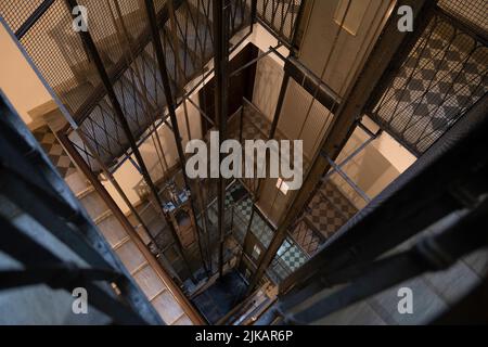 Plan spectaculaire d'un escalier qui regarde dans un ascenseur avec des tiges métalliques, des câbles et une cabine dans un immeuble d'appartements d'époque à Rome Banque D'Images