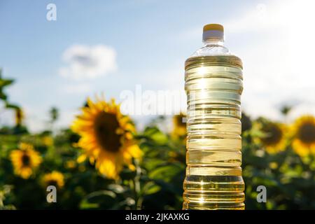 Bouteille en plastique d'huile de tournesol dorée fraîche au coucher du soleil. Champ de fleurs de soleil sur le fond. Banque D'Images