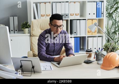 Jeune ingénieur vietnamien travaillant sur ordinateur portable dans son bureau Banque D'Images