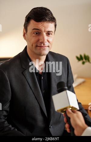 Homme politique positif et réussi donnant une interview au journaliste et parlant en micro Banque D'Images