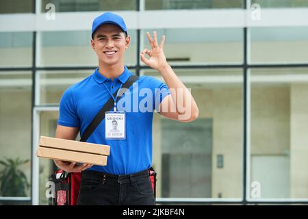 Portrait d'un jeune livreur élégant avec deux boîtes à pizza montrant le panneau ok Banque D'Images