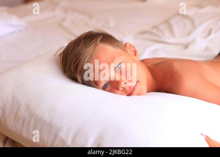 Un garçon se trouve sur un lit avec des draps blancs dans une chambre d'hôtel. L'enfant dort. Adolescent au lit à la maison Banque D'Images