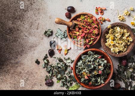 Bols en bois aux herbes médicinales : menthe, framboise, rosehip, coing, camomille et rose, arrière-plan sombre. Herbes séchées de médecine alternative, en bonne santé Banque D'Images