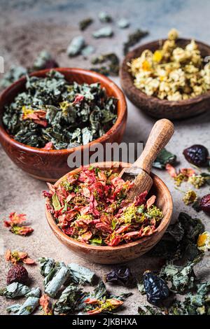 Bols en bois aux herbes médicinales : menthe, framboise, rosehip, coing, camomille et rose, arrière-plan sombre. Herbes séchées de médecine alternative, en bonne santé Banque D'Images