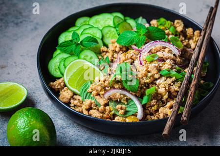 Salade de poulet thaï larb gai avec oignon, concombre et menthe dans une assiette noire. Concept alimentaire asiatique. Banque D'Images