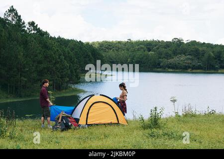 Campeurs mettant la tente sur la prairie au bord du lac Banque D'Images