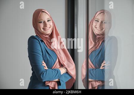 Portrait d'une femme d'affaires souriante portant le hijab au bureau près d'une fenêtre. Banque D'Images
