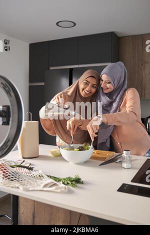 Deux bûcherons musulmans souriant tout en versant de l'huile d'olive dans une salade dans la cuisine. Banque D'Images