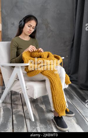 Portrait d'une femme portant un casque tricoter à la maison, assis sur un fauteuil confortable dans le salon, heureuse positive femme appréciant le temps de loisirs, tenue Banque D'Images
