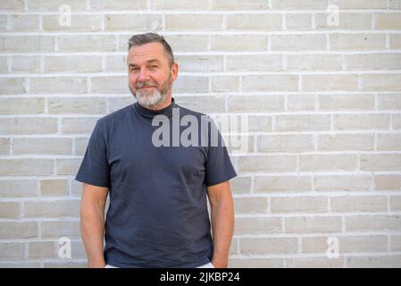 Homme amusé regardant la caméra avec un sourire en regardant devant un mur de briques blanches Banque D'Images