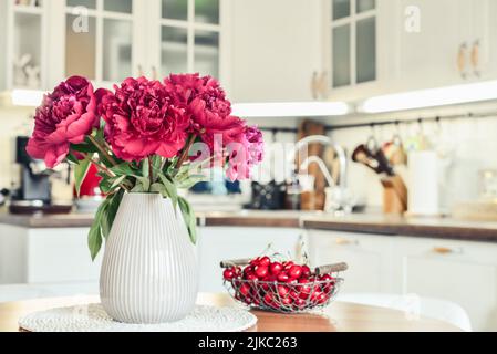 Bouquet de fleurs de pivoines violettes à l'intérieur de la cuisine de style scandinave avec mobilier blanc. Banque D'Images