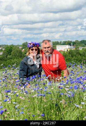 couple marié au milieu d'un champ coloré de cornflowers appréciant l'été, ciel plein de nuages, paysage ensoleillé d'été Banque D'Images