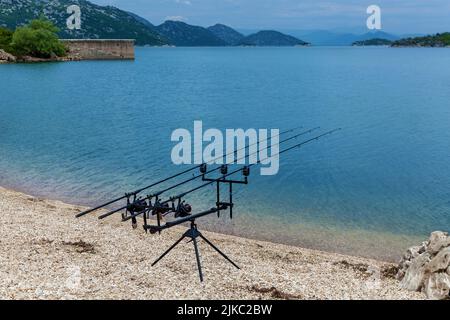 Vous trouverez des cannes à pêche sur la plage de sable du lac, sur fond de montagnes Banque D'Images