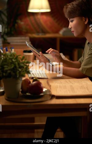 Jeune femme asiatique utilisant une tablette numérique tout en étudiant à la maison le soir Banque D'Images