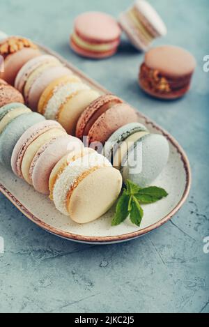 Macarons français colorés sur plaque sur fond bleu Banque D'Images