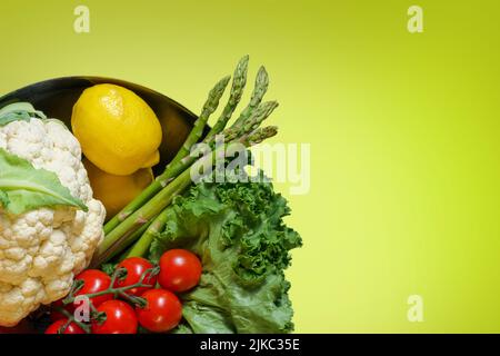 Bol de légumes frais biologiques, salade, chou-fleur, tomate, citron, Asperges, carotte sur fond jaune avec espace copie, concept alimentaire Healsy Banque D'Images