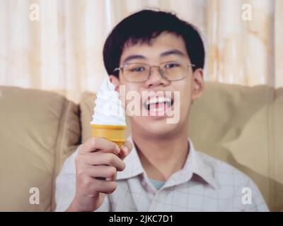 Un enfant d'Asie tient la glace à la vanille dans le cône de gaufres heureux souriant et manger délicieusement en été avec plaisir et bonne humeur. Banque D'Images