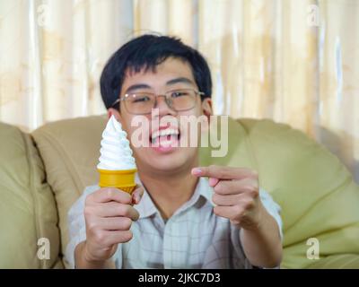 Un enfant d'Asie tient la glace à la vanille dans le cône de gaufres heureux souriant et manger délicieusement en été avec plaisir et bonne humeur. Banque D'Images