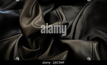 La texture de la veste en cuir à plis noirs produit des contrastes de lumière et d'ombre Banque D'Images