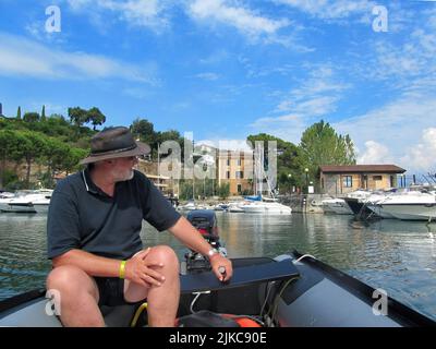 homme conduisant un bateau gonflable avec hors-bord devant une marina Banque D'Images