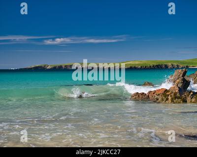 Les vagues se brisent dans l'eau turquoise claire sur une plage près de Scousburgh dans le sud de Shetland, Royaume-Uni. Pris par une journée ensoleillée avec un ciel bleu. Banque D'Images