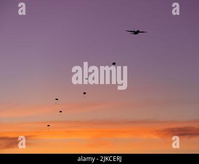 Une silhouette d'avion et de parachutes contre un magnifique ciel de pêche au coucher du soleil Banque D'Images