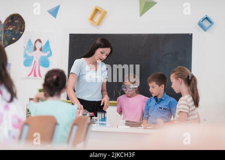 École élémentaire de sciences en classe : un professeur enthousiaste explique la chimie à divers groupes d'enfants, produits chimiques de mélanges de petits garçons dans les béchers Banque D'Images