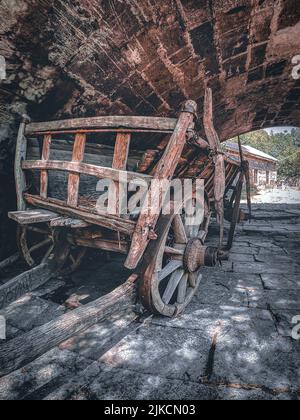 Une photo verticale d'une charrette en bois Vintage sous une arche de pierre dans un vieux village. Banque D'Images