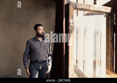 Un jeune homme barbu en costume regarde par la fenêtre Banque D'Images