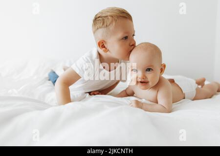 un petit frère embrasse et embrasse sa sœur, un nouveau-né. L'enfant rencontre un nouveau membre de la famille. Un garçon mignon et une fille de nouveau-né sont relaxants Banque D'Images