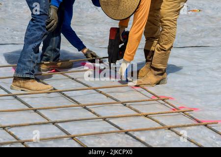 Dans le cadre du processus de construction de fondations de ciment, un ouvrier de construction utilise un outil de ficelage de barre d'armature pour tordre les barres d'acier avec le renforcement de tige de fil. Banque D'Images