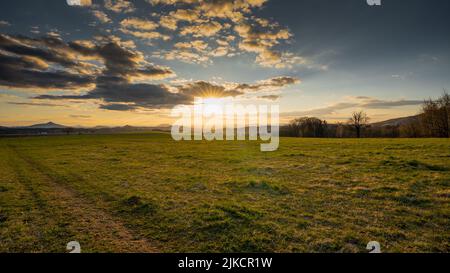 Coucher de soleil romantique sur un champ dans le nord de la Bohême. Le ciel est calme et avec peu de nuages et de soleil au-dessus de l'horizon. Banque D'Images