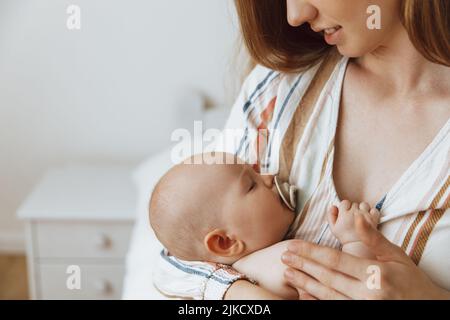 Une mère aimante prend soin de son nouveau-né à la maison. Portrait d'une mère heureuse tenant un bébé endormi dans ses bras. La mère embrassait son petit bab Banque D'Images