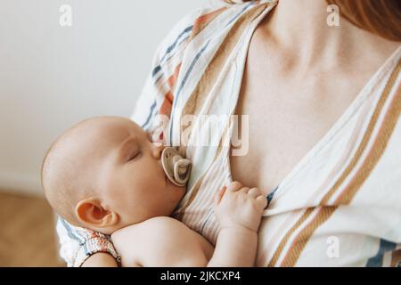 Une mère aimante prend soin de son nouveau-né à la maison. Portrait d'une mère heureuse tenant un bébé endormi dans ses bras. La mère embrassait son petit bab Banque D'Images