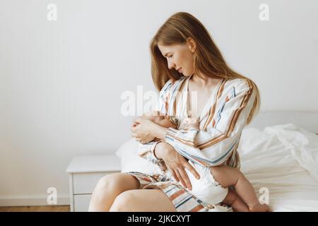 Une mère aimante prend soin de son nouveau-né à la maison. Portrait d'une mère heureuse tenant un bébé endormi dans ses bras. La mère embrassait son petit bab Banque D'Images