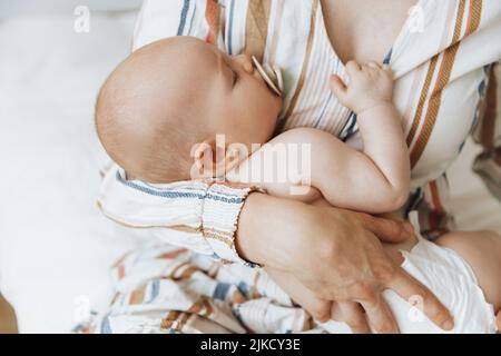 Une mère aimante prend soin de son nouveau-né à la maison. Portrait d'une mère heureuse tenant un bébé endormi dans ses bras. La mère embrassait son petit bab Banque D'Images