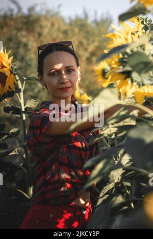 Une jeune fille dans un champ de tournesols au coucher du soleil. Portrait d'une femme avec une silhouette mince sur un fond de fleurs jaunes Banque D'Images