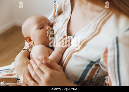 Une mère aimante prend soin de son nouveau-né à la maison. Portrait d'une mère heureuse tenant un bébé endormi dans ses bras. La mère embrassait son petit bab Banque D'Images