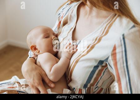 Une mère aimante prend soin de son nouveau-né à la maison. Portrait d'une mère heureuse tenant un bébé endormi dans ses bras. La mère embrassait son petit bab Banque D'Images