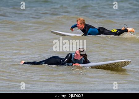 Femme surfeuse en combinaison couchée et attendant sur sa planche de surf pour une grande vague / brise-roches sur la côte de la mer du Nord Banque D'Images