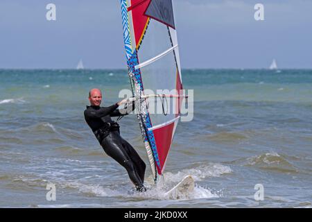 Planche à voile sportive en combinaison noire pratiquant la planche à voile classique le long de la côte de la mer du Nord Banque D'Images