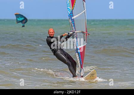 Planche à voile sportive en combinaison noire pratiquant la planche à voile classique le long de la côte de la mer du Nord Banque D'Images